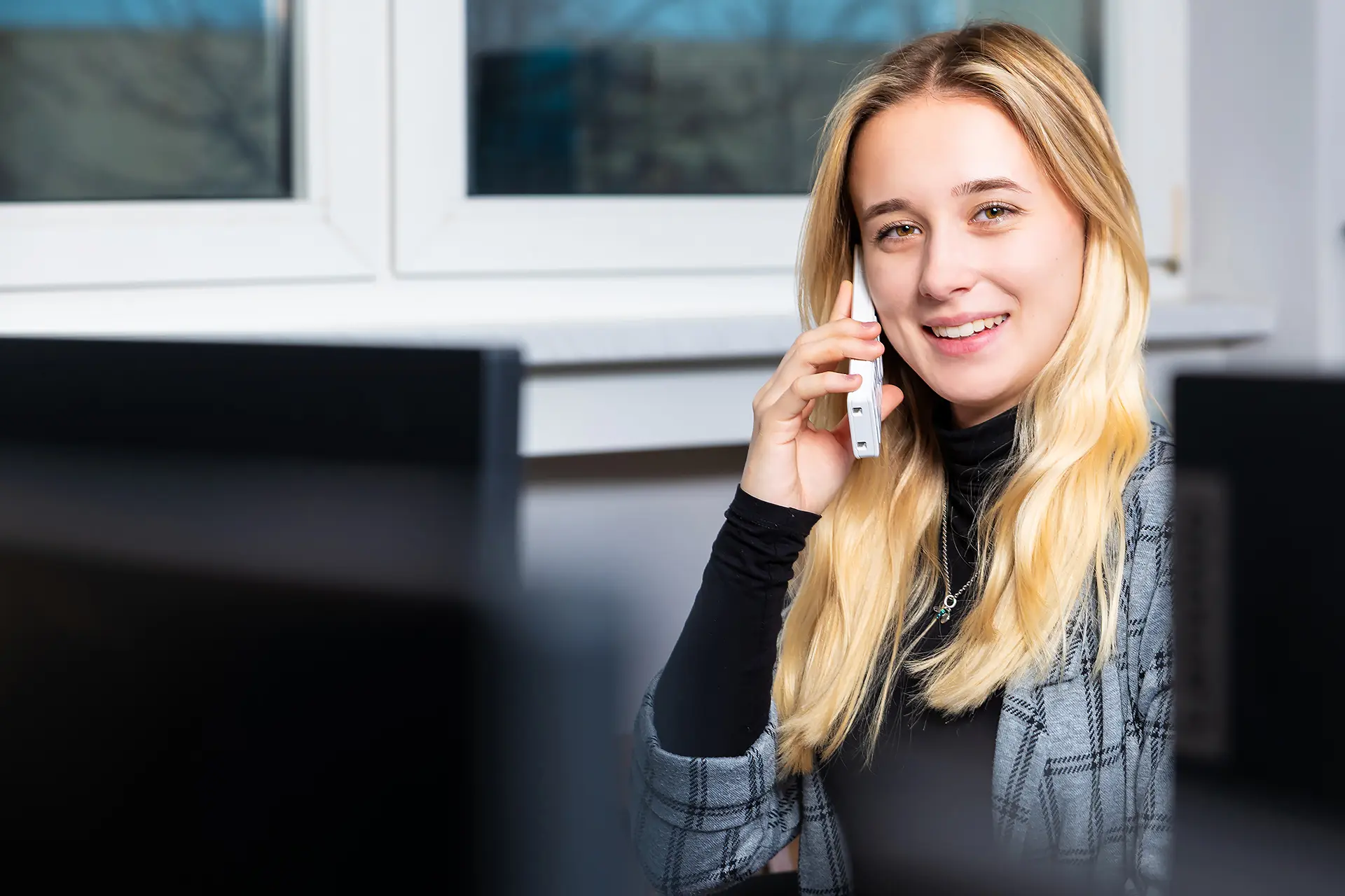 Freundliche Mitarbeiterin der i-Arbeitsschutz Service GmbH telefoniert lächelnd mit einem Kunden im Büro, um ihn zum Thema Arbeitssicherheit zu beraten.