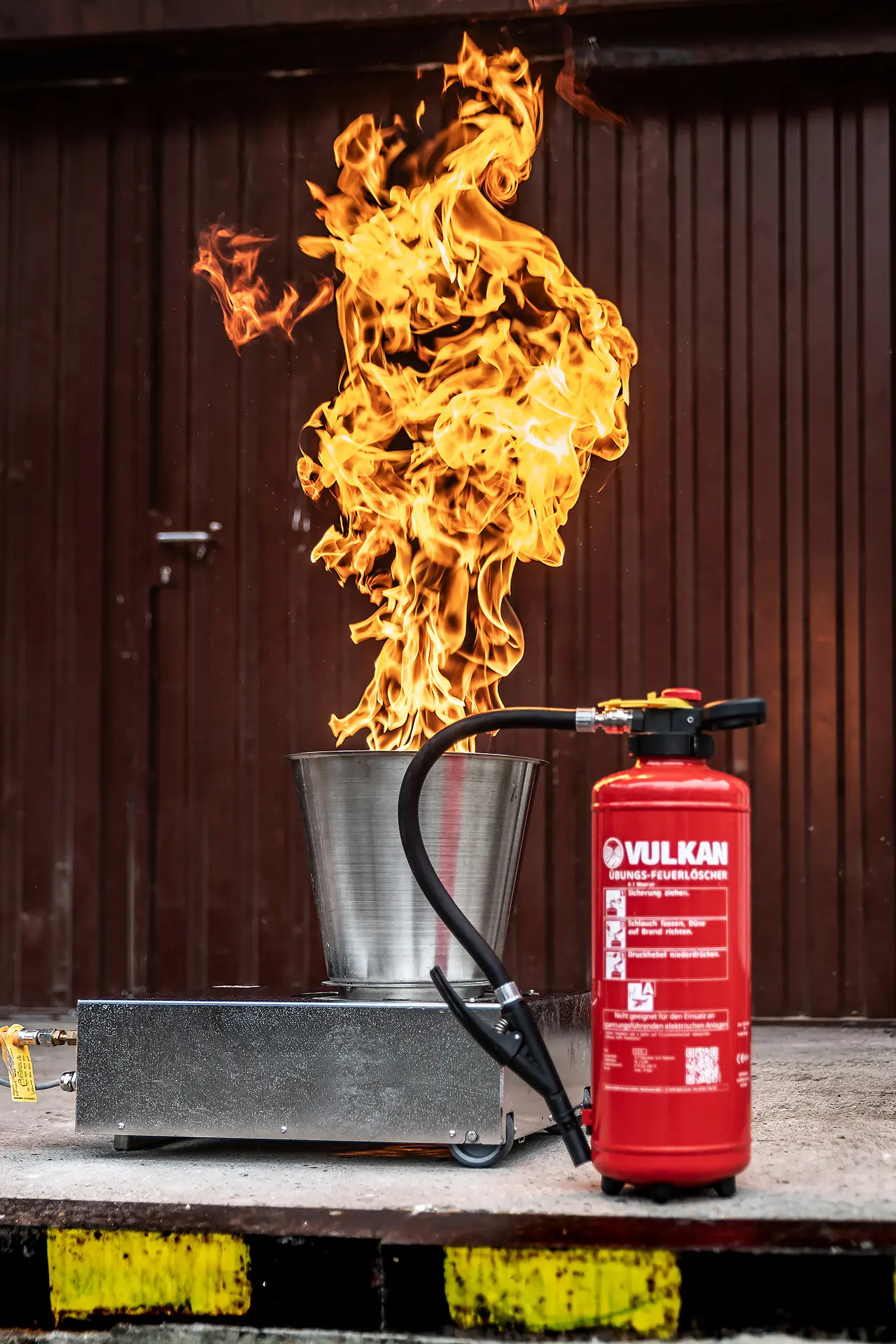 Roter Feuerlöscher vor einem lodernden Feuer bei einem praktischen Feuerlöschtraining für den betrieblichen Brandschutz der i-Arbeitsschutz Service GmbH.