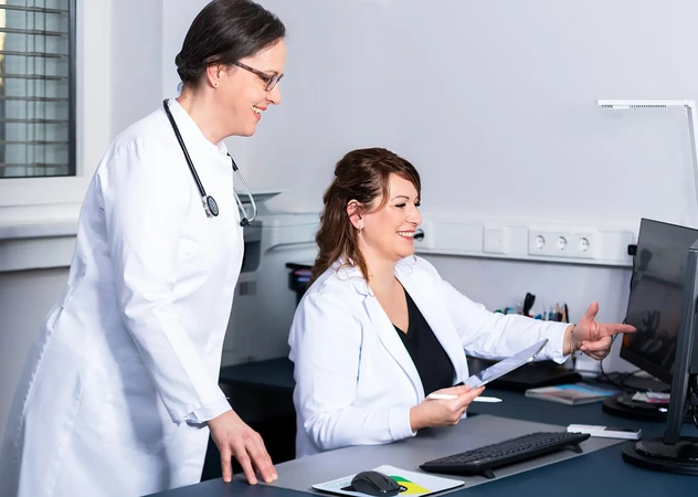 Betriebsärztin und medizinische Fachangestellte der i-Arbeitsschutz besprechen gemeinsam digitale Gesundheitsdaten am Computer für die arbeitsmedizinische Betreuung.